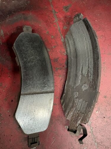 Two worn brake pads with metal retaining clips heavy wear on the friction material.